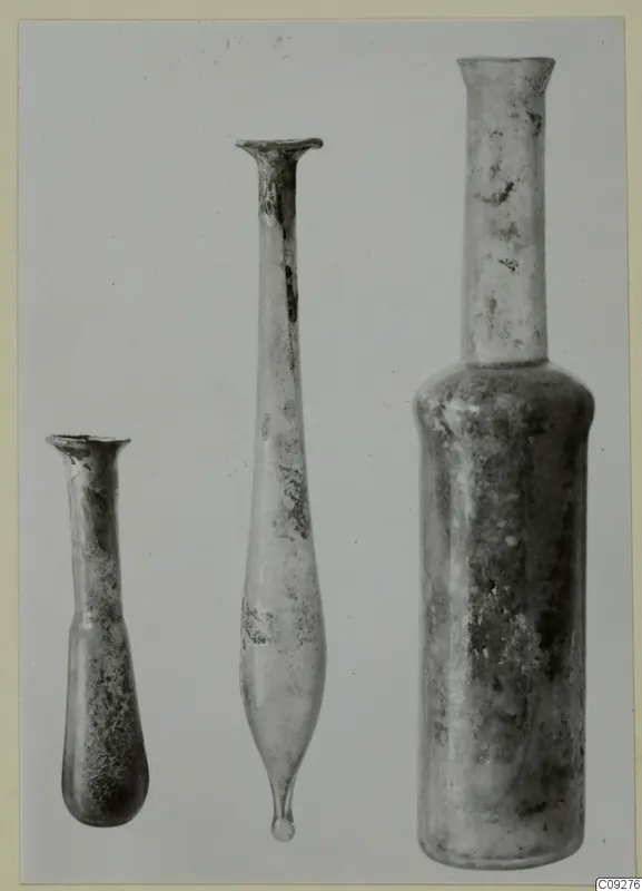 Three blown glass bottles, flasks and unguentaria standing in a row against a plain background