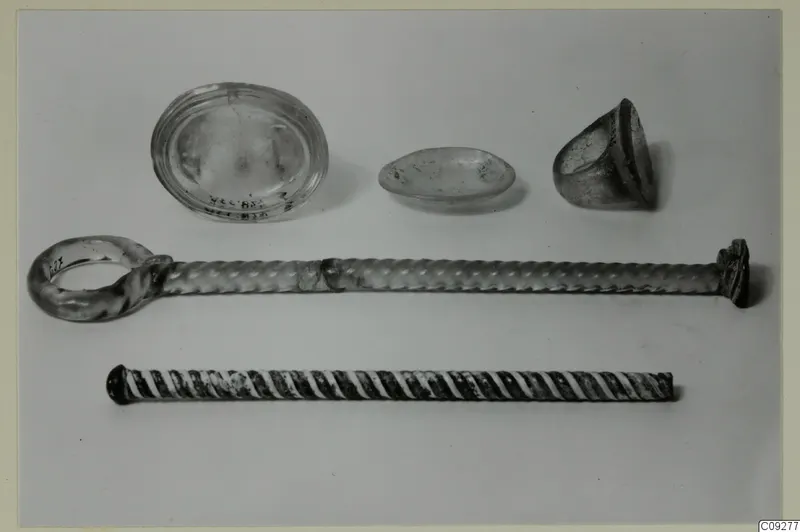 Five small objects on a light surface: an oval glass dish, a shallow dish, a cup fragment and two twisted rods, one with a ring at one end.