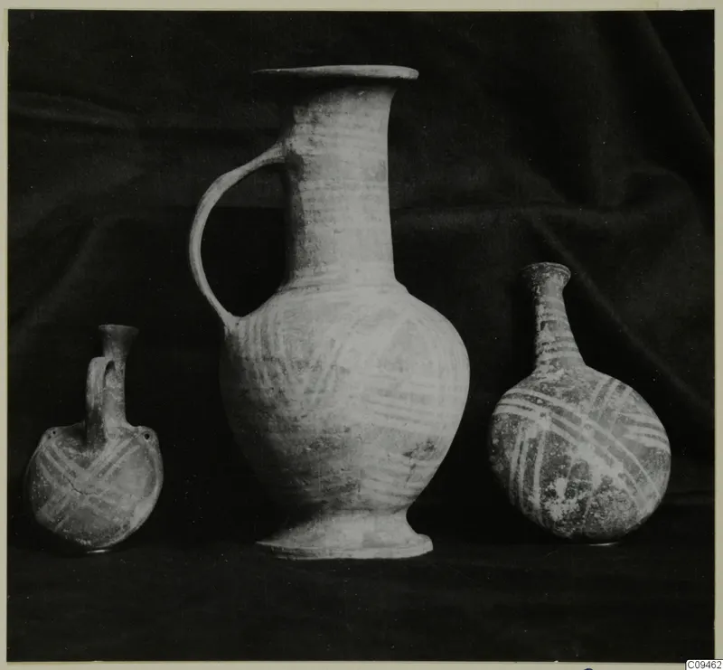 Three painted pottery vessels, a small flask, a tall jug and a bottle, standing on a dark draped cloth.