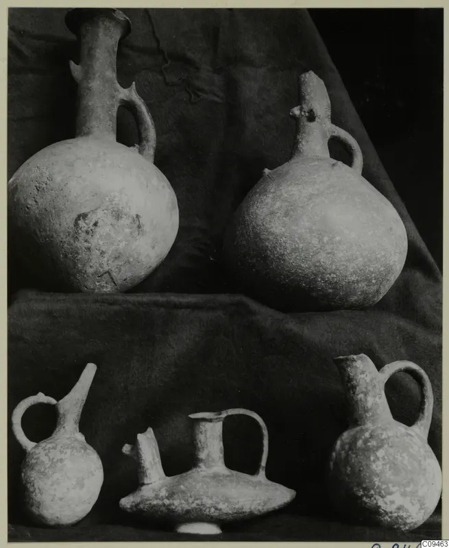 Five pottery jugs and juglets with handles and spouts, grouped on a dark cloth.