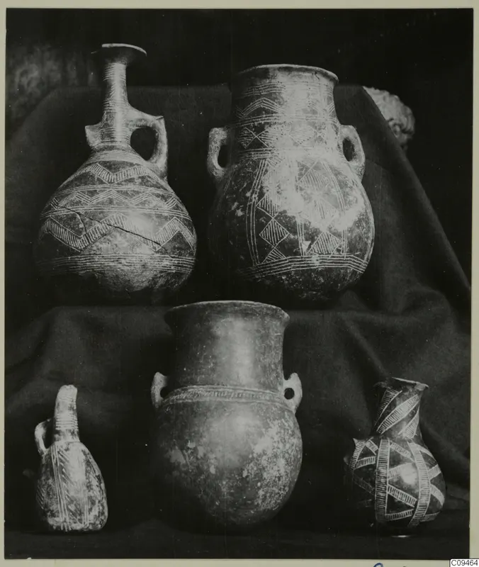 Five pottery vessels, jugs and jars with painted and relief decoration, grouped on dark draped cloth