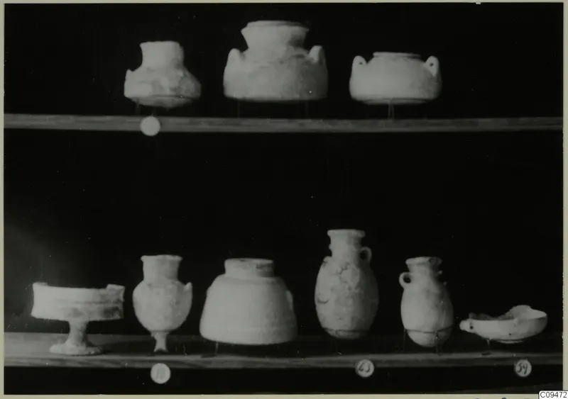 Several small pottery vessels and bowls standing on two wooden shelves against a black background.
