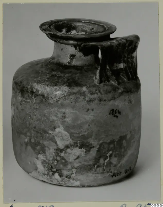 Blown glass jug with a flared rim and a ribbed handle, weathered and clouded.