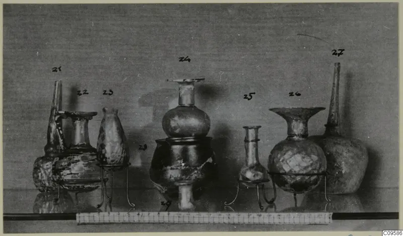 Several blown glass vessels on wire stands, with handwritten number labels and a scale ruler along the front