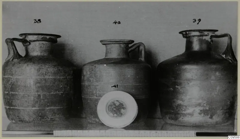 Three jugs with handles photographed in a row, with number labels and a white round dish in front