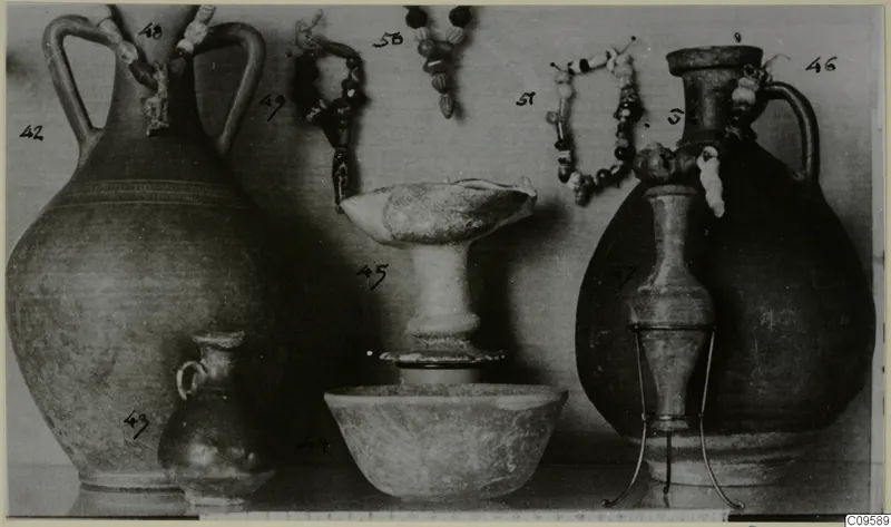 Group of vessels: two two-handled jugs, a small juglet, a stemmed dish and a bowl, with bead strands hanging behind.
