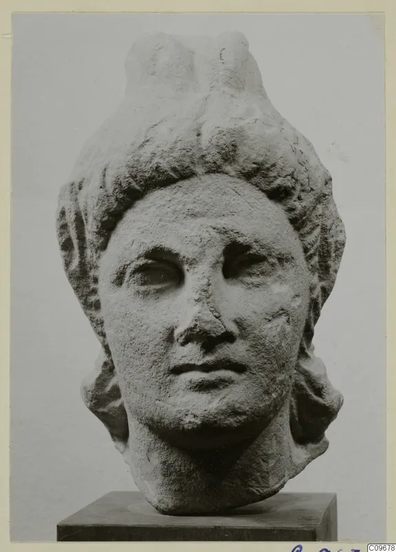 Carved stone head sculpture with elaborate hair and a raised crest, shown on a dark square base
