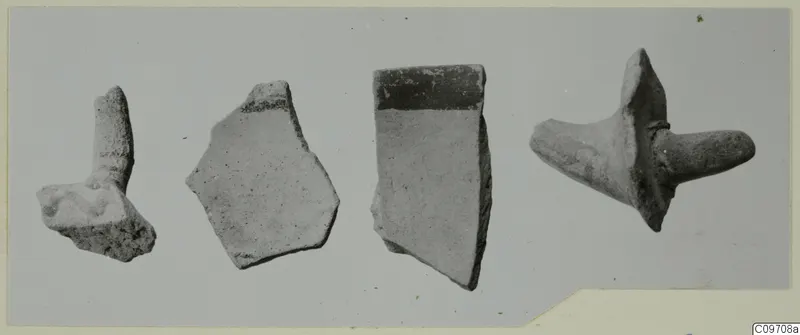 Four pottery sherds lying in a row on a grey surface, one with a projecting lug.