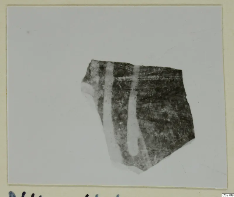 Pottery sherd from Nitovikla with two pale vertical bands on a dark surface, shown on a card mount.