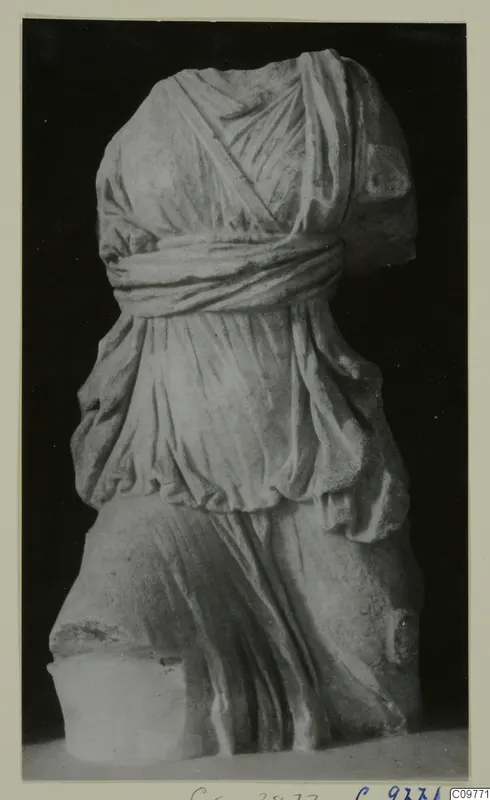Headless draped statue torso in pale stone, photographed against a black background