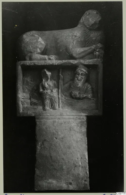 Carved stone object with a recumbent animal on top and a relief panel showing two seated figures