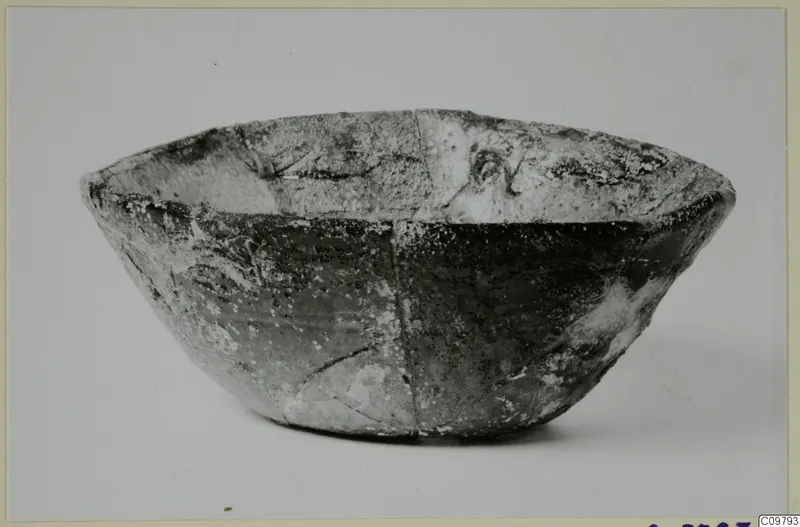 Deep rounded bowl with a flared rim, cracked and pale-encrusted, shown side-on against a plain background