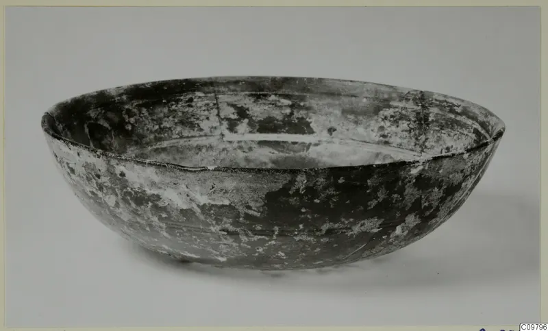 Cast glass bowl, shallow with rounded sides and pale weathered patches on a dark surface