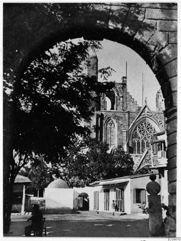 Ruined St Nicholas Cathedral in Famagusta seen through a stone archway, with trees and people in the street below
