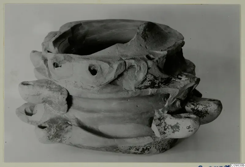 Terracotta lamp with a wide open top and several rounded projecting nozzles, some with holes.