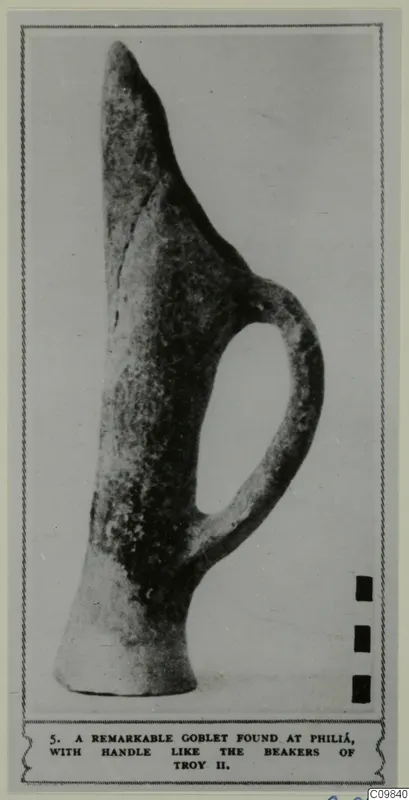 Pottery vessel with a tall pointed neck, a single loop handle and a wide flat base, shown in a photo mounted on a printed page