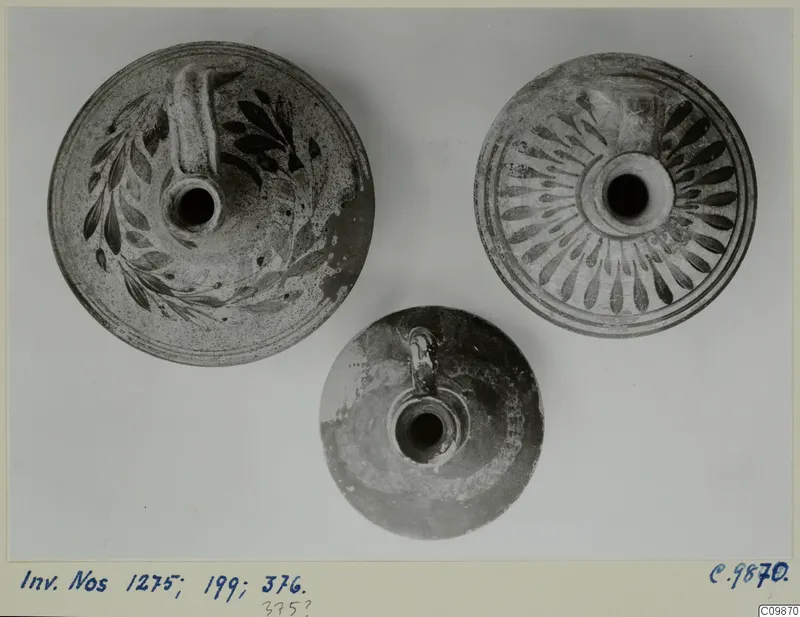 Three pottery vessels with handles and central openings, seen from above; two have dark painted patterns.