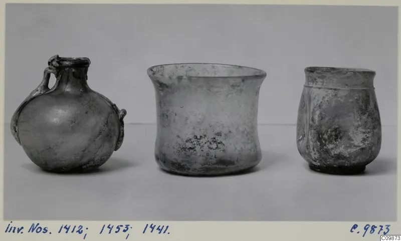 Three vessels of different shapes standing in a row on a pale surface against a grey backdrop