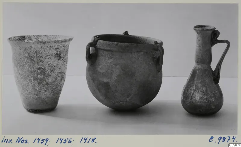 Three weathered vessels side by side: a flared beaker, a round two-handled pot and a small jug with a looped handle.