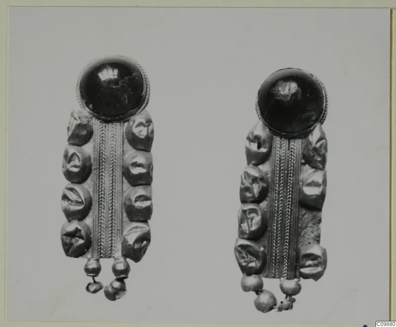 Two matching pieces of jewellery, each with a dark domed stone or glass top and a beaded metal plate, shown side by side