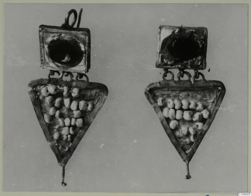 Pair of jewellery pieces: square plates with dark centres above triangular frames holding pale beads, on a grey background.
