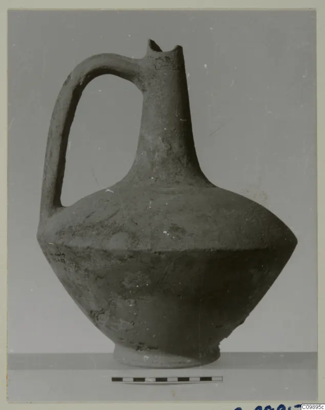 Pottery jug with a strap handle, broken rim and ring base, shown beside a scale bar