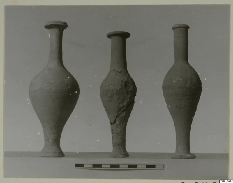 Three pottery jars with long necks standing in a row, with a scale bar in front