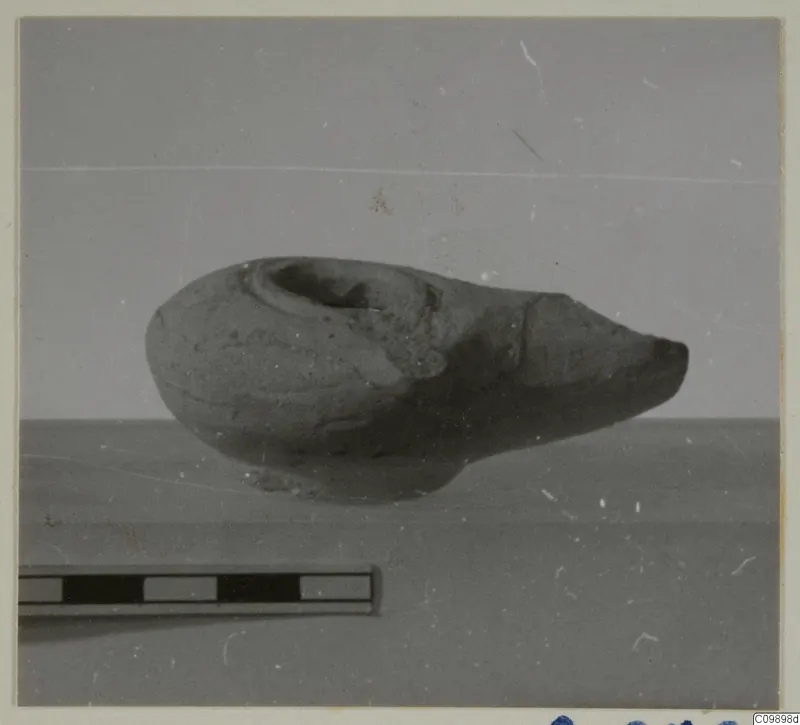 Clay oil lamp with a pointed nozzle to the right, shown beside a scale bar