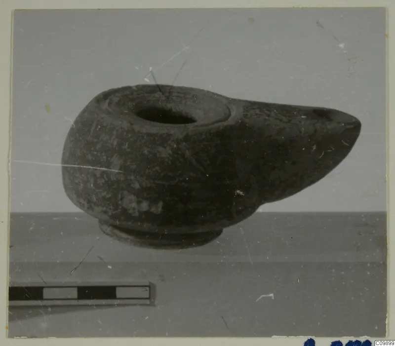 Pottery lamp with a projecting spout and round filling hole, photographed beside a scale bar