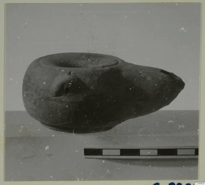 Dark vessel with a wide mouth and tapering spout, photographed on a surface beside a scale bar.