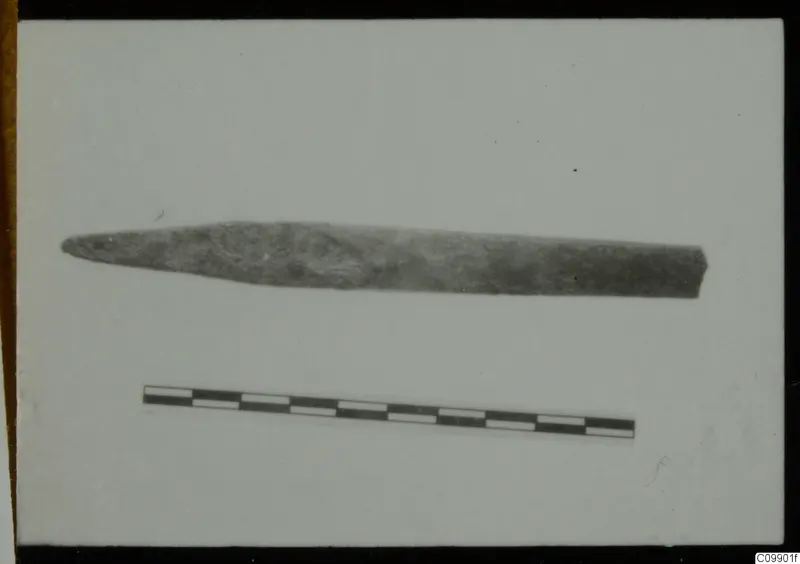 Long, pointed corroded metal object, possibly a tool, with a scale bar below it
