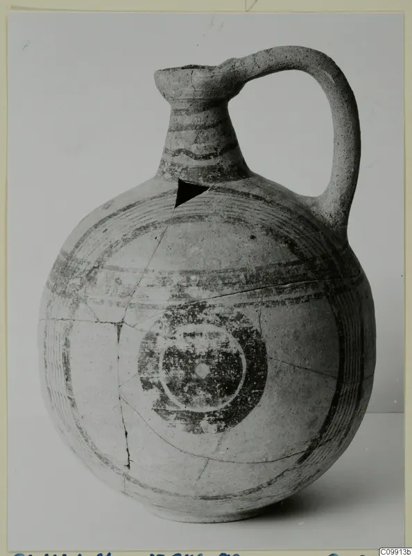 Bichrome V jug with a tall neck, strap handle, painted bands and a dark ring motif on the body