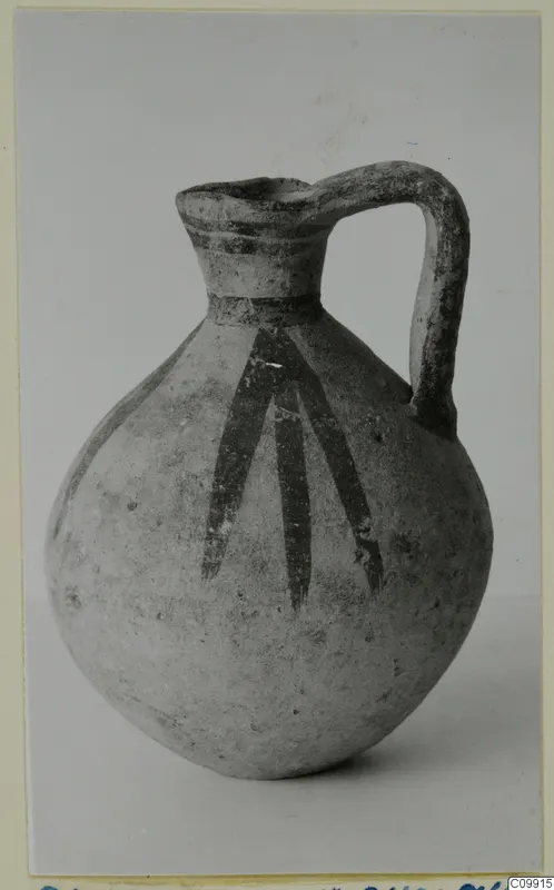 Pottery Bichrome V jug with a strap handle and dark painted strokes running down the body