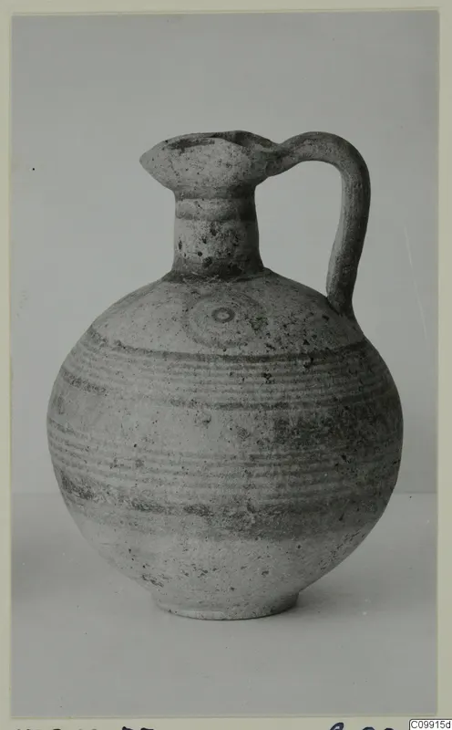 Round-bodied jug with a trefoil-like mouth and strap handle, painted with horizontal bands and a circular motif.