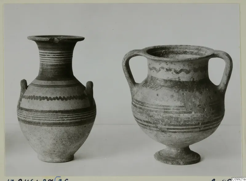 Two painted pottery vessels with handles, one with a flared neck and one standing on a low foot, against a plain background
