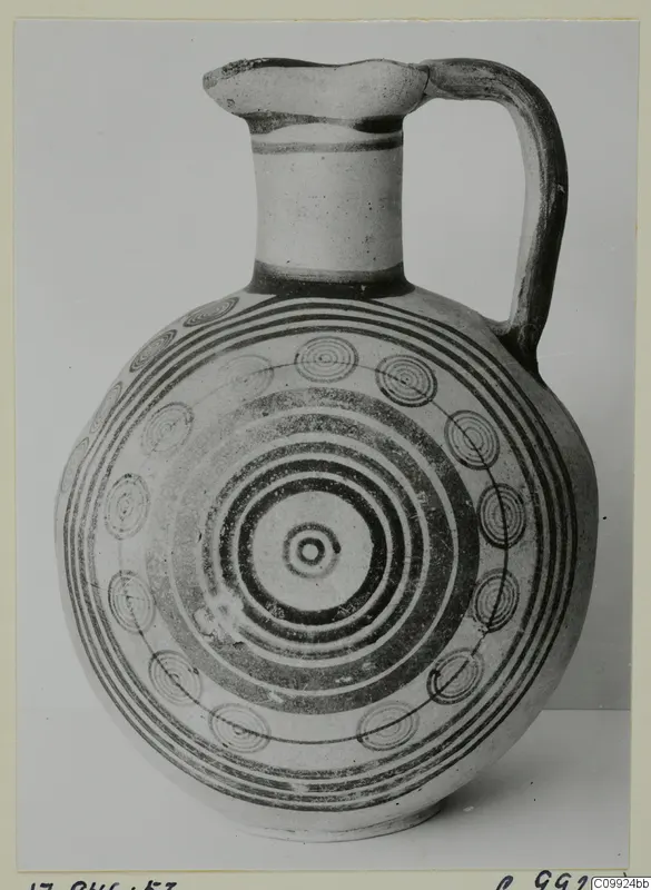 Jug with a tall neck, strap handle and concentric circle decoration painted in dark bands on its rounded body