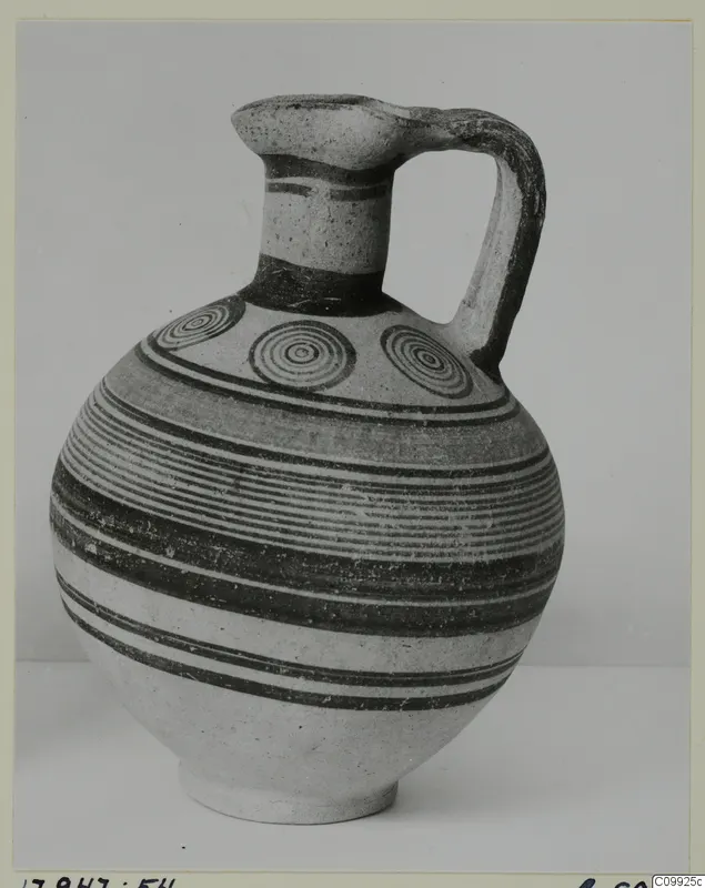 Jug with a strap handle, horizontal painted bands and concentric circles on the shoulder, photographed against a plain backdrop.