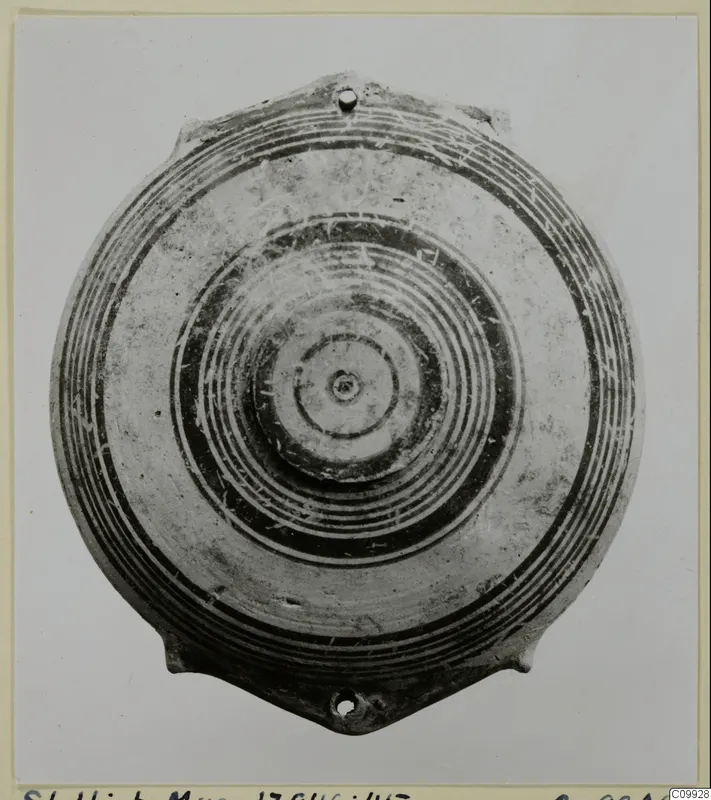 Pottery Bichrome IV plate with concentric painted rings and two small pierced lugs, seen from above