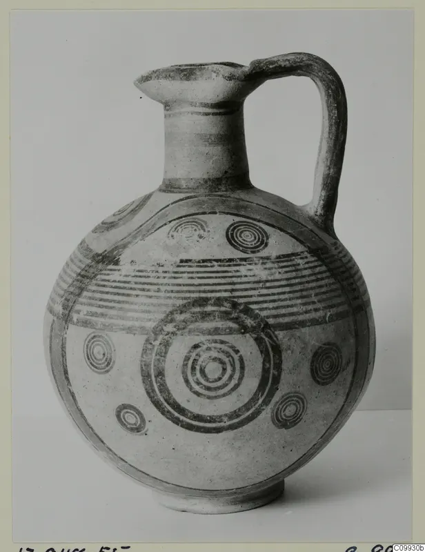 Round-bodied jug with a high loop handle and concentric circle and banded painted decoration in dark paint.