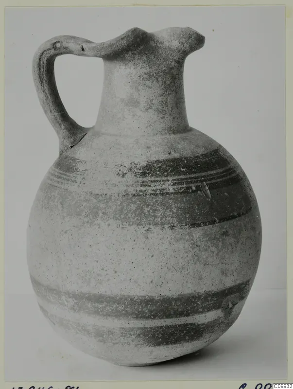 Bichrome IV jug with a handle and trefoil-like spout, decorated with dark painted bands on a pale body.
