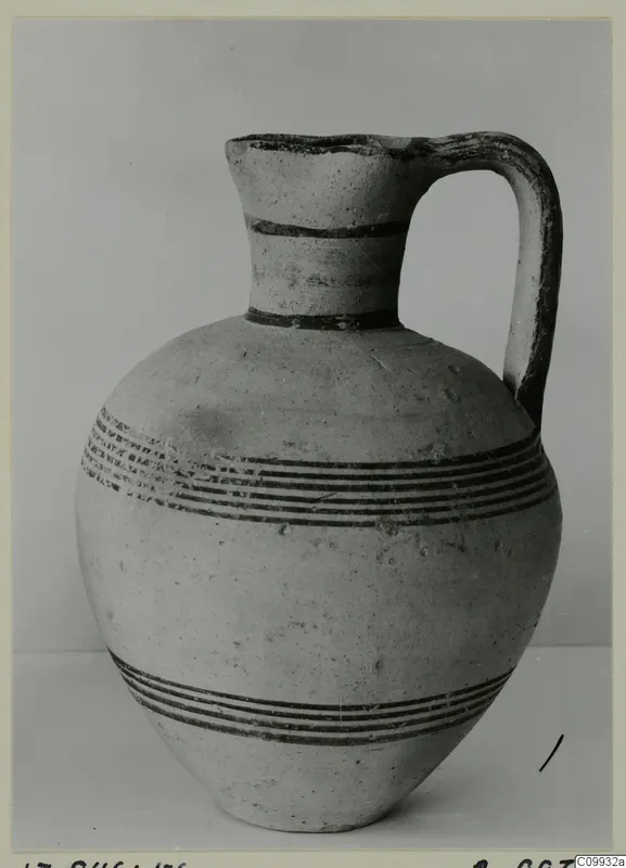 Pale pottery jug with a single strap handle and dark painted bands, photographed against a grey backdrop