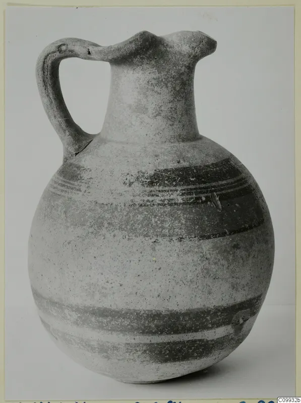 Bichrome V jug with a round body, long neck, strap handle and dark painted bands