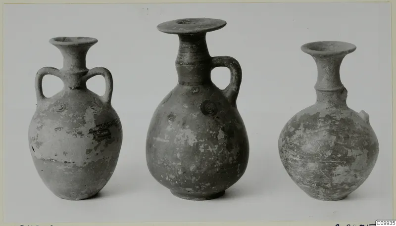 Three pottery vessels with flared rims, the left one with two handles, photographed side by side on a plain background