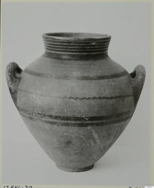 Two-handled jar with dark painted bands and fine rings, photographed against a plain grey background