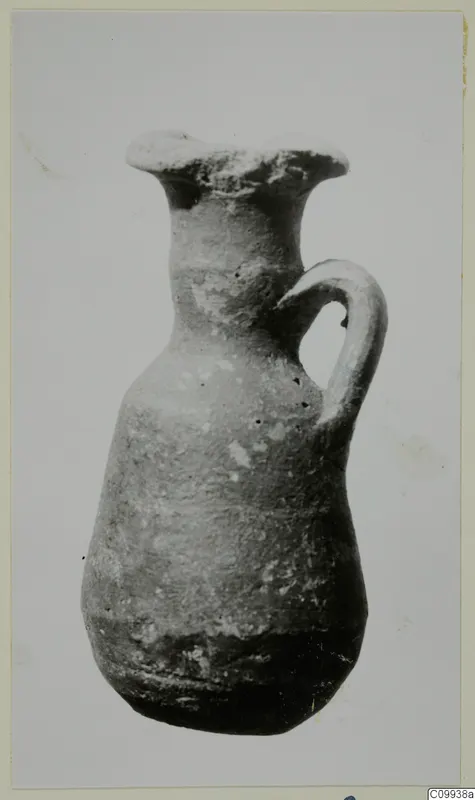 Small pottery jug with a flared mouth and a single strap handle, photographed against a plain background.