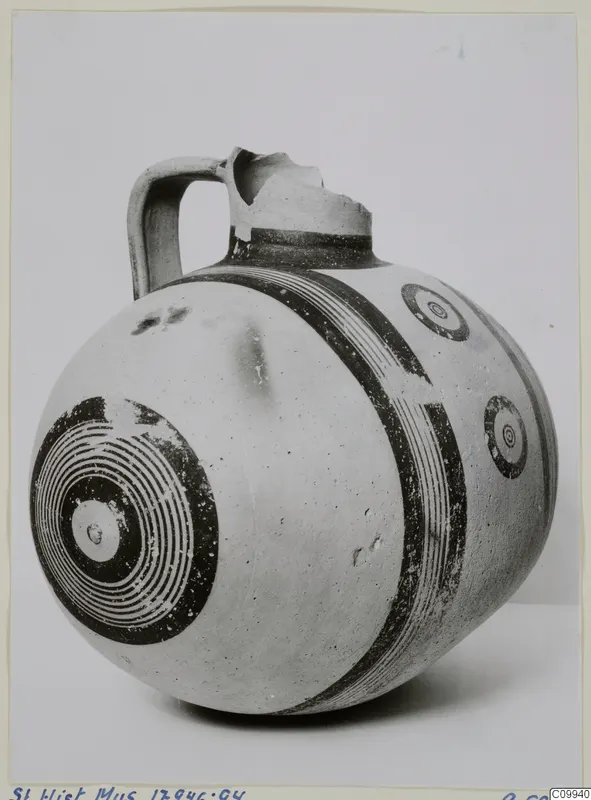 White Painted V jug with a single strap handle, broken neck and rim, and dark bands and concentric circles