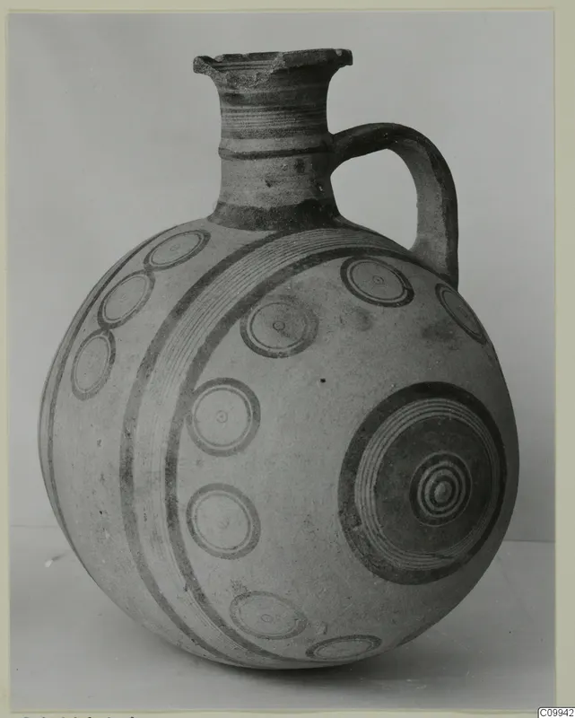 Globular jug with a short neck, single strap handle and dark painted concentric circles and bands on a pale surface
