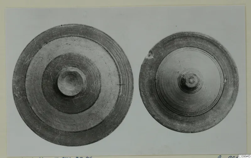 Two round pottery objects seen from above, one larger, both with concentric grooves and a central knob.