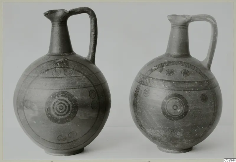 Two painted pottery jugs with a single handle, decorated with black concentric circles and horizontal bands.