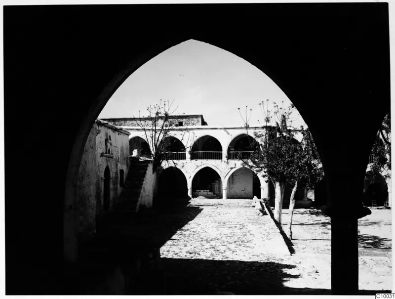 Courtyard of a monastery building seen through a pointed archway, with an outside staircase and bare trees